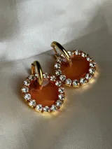 Par de aros colgantes con dije circular de resina con glitter multicolor y borde de strass. El arito es de acero quirúrgico dorado.