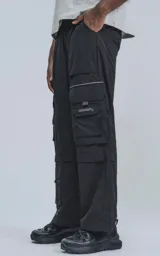 Pantalón negro de corte ancho con cintura elástica, múltiples bolsillos y detalles reflectivos.