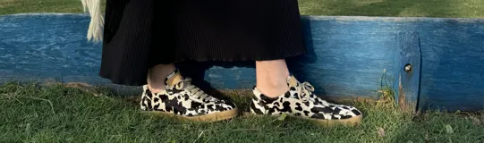 Zapatillas bajas con estampado animal print de vaca en blanco y negro, con cordones marrones y suela color caramelo.