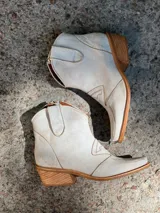 Botas cortas de cuero sintético color beige con detalles de costuras estilo western.