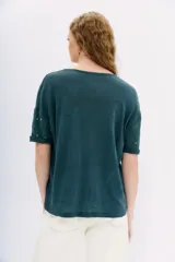 Remera blanca de lino con tachas plateadas en el frente, cuello redondo y mangas cortas.