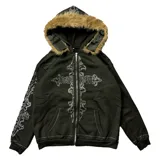 Campera negra con cierre frontal, capucha con borde de piel sintética removible, bolsillos laterales y apliques de strass plateados formando una cruz en el frente y diseños ornamentales en las mangas.