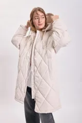 Campera larga color crudo con capucha y cierre frontal, diseño acolchado con patrón de rombos.