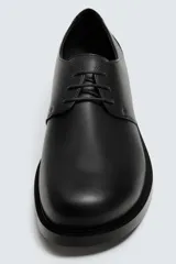 Zapato de vestir de cuero negro, tipo derby con cordones, de horma redonda y suela con ligero tacón.
