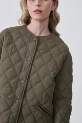 Campera acolchada negra, con diseño capitoné en rombos, cuello redondo y cierre frontal con botones a presión. Posee bolsillos delanteros amplios.