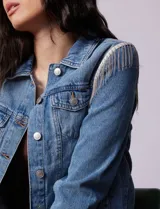 Campera de jean celeste de la marca Baccini, con cierre central, bolsillos delanteros, apliques colgantes de tachas en los hombros y terminación desflecada en el ruedo.