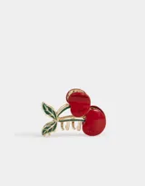 Broche para el pelo dorado con forma de cerezas rojas y hojas verdes.