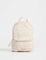 Mochila pequeña de cuerina color crema con estampado de flores pequeñas en tonos rosa, naranja y celeste. Tiene un bolsillo frontal con cierre, correas regulables, manija superior, cierre superior y bolsillos laterales.