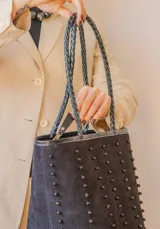 Cartera tote negra de cuero con forro interior y tachas redondas en filas verticales. Asas de cuero trenzado.