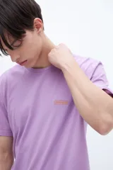 Remera de manga corta color lila con cuello redondo y parche con texto en el pecho.