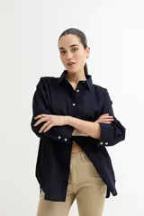 Camisa blanca de corte amplio, con cuello clásico, cierre frontal con botones y mangas largas con puños abotonados.