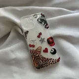 Funda transparente para celular con múltiples stickers decorativos incrustados o adheridos, incluyendo un primer plano de un leopardo, cerezas, labios rojos, un corazón rojo, una bola de billar 8, una estrella con estampado de leopardo y otros motivos pequeños.