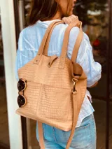 Cartera tipo tote bag color beige con textura símil cocodrilo, doble asa corta y correa larga extraíble y ajustable. Tiene dos bolsillos externos grandes y cierre superior con botón a presión.