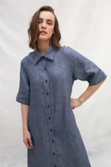 Vestido camisero midi color beige, de lino, con abotonadura frontal completa, manga ranglan, bolsillos laterales y un volante en el ruedo.