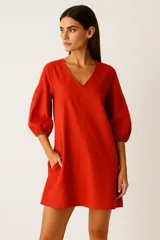 Vestido corto color ladrillo, de lino, con escote en V y mangas 3/4 abullonadas con puño elástico. Posee bolsillos laterales.