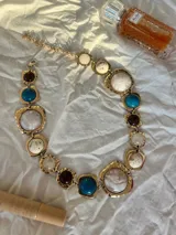 Collar dorado con eslabones grandes y piedras de colores: azul, marrón, blanco y crema.