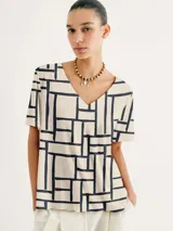 Blusa de corte holgado con estampado geométrico en negro sobre fondo blanco y escote en V.