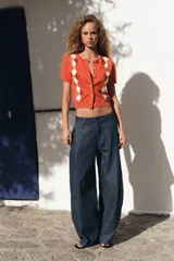 Chaqueta de punto color naranja con cuello redondo y manga corta. Presenta cierre frontal con botones y estampado de rombos en tonos blanco, naranja y marrón.