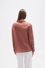 Camisa blanca de broderie con cuello camisero, cierre frontal de botones, mangas largas y corte holgado.