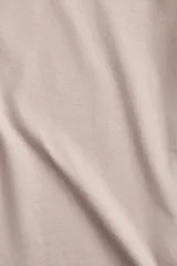 Remera color beige de corte recto en punto suave de algodón con cuello redondo ribeteado y hombros ligeramente caídos.