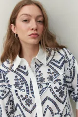 Camisa blanca de manga larga con bordado floral marrón, cuello clásico y cierre frontal con botones.