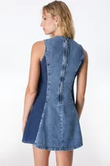 Vestido corto sin mangas de denim color marrón con efecto lavado. Presenta corte en A, cuello redondo, cierre trasero y detalle de tachas doradas en los laterales. El ruedo tiene terminación desflecada.