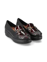 Mocasín de cuero charol negro con plataforma blanca y detalle de hebilla metálica plateada en el empeine.