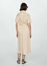 Vestido camisero midi color beige, de tela satinada, con cuello camisero, mangas cortas, dos bolsillos de parche en el pecho, lazo ajustable en la cintura y cierre frontal con botones.