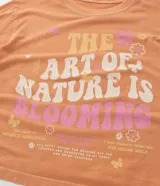 Remera color durazno de corte cuadrado con cuello redondo y mangas cortas. Estampa frontal con flores y la frase "The art of nature is blooming".