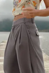 Pantalón negro de tiro alto con trabillas, doble pliegue, bolsillos laterales y tapetas en la espalda. Tiene pernera ancha y cierre frontal con cremallera y gancho metálico.