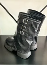 Botas negras de caña media con suela track y tres hebillas decorativas.