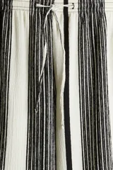 Pantalón palazzo de punto con textura a rayas verticales en blanco y negro. Tiene tiro alto, piernas rectas, elástico en la cintura y cordón para ajustar.