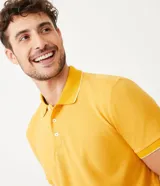 Polo de manga corta color amarillo, confeccionada en tejido de piqué con cuello clásico y tapeta de dos botones. Presenta ribetes blancos en cuello y mangas.