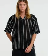 Camisa masculina modelo boxy, confeccionada en punto, con cuello polo, manga corta, cierre por botones y estampa de rayas verticales blancas sobre fondo negro.