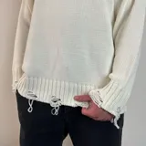 Sweater tejido color crema con cuello redondo y terminaciones con efecto desgastado y roturas.