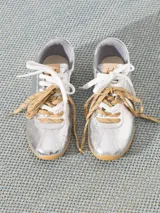 Zapatilla plateada de cuero vacuno con recortes en cuero descarne, doble cordón (uno blanco y otro marrón con pintitas) y charms colgantes.