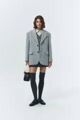 Blazer de lana con mezcla de alpaca en color gris claro, con cuello sastre, cierre frontal de dos botones y bolsillos laterales con solapa. Presenta una textura suave y ligeramente vellosa que aporta calidez.