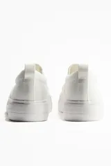 Zapatillas slip-on blancas de lona con elásticos laterales, cuello acolchado y tirador trasero.