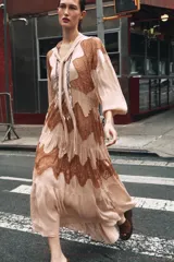 Vestido midi color beige con detalles de encaje marrón, cuello alto con lazo, escote pico, manga larga y botones frontales.