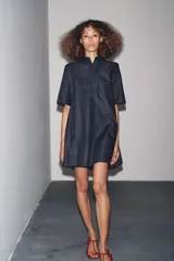 Vestido corto de Zara Woman Collection confeccionado en tejido tipo denim. Tiene cuello solapa, manga corta, bolsillos delanteros ocultos, bajo evasé y cierre frontal con botones.