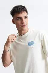 Remera de manga corta color crudo, de corte oversize con estampado de flor azul y texto "blurred Mistral".