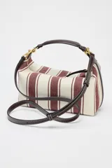 Bolso de mano tipo city, confeccionado en tejido con estampado de rayas verticales en tonos crudo y bordó. Tiene doble correa de hombro extraíble en contraste de tejidos, detalles metálicos y cierre mediante cremallera.