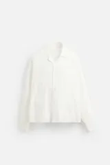 Camisa blanca de corte relaxed fit confeccionada en tejido de algodón y lino. Tiene cuello bowling, manga larga con puños abotonados, jaretas en el delantero, bolsillos de parche en pecho y cadera, bajo con aberturas laterales y cierre frontal con botones.