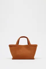 Bolso mini shopper color marrón de serraje, con asa de mano y asa bandolera extraíble. Tiene detalle de pespunte en el corte, bolsillo interior y cierre mediante mosquetón.