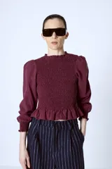 Blusa color borgoña con escote redondo con volados, mangas largas abullonadas y cuerpo fruncido.
