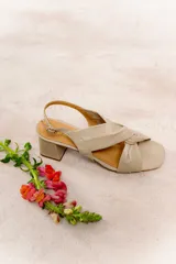 Sandalia de cuero color beige, con tiras anchas cruzadas y detalle de nudo central. Tiene pulsera regulable en el talón y taco ancho de 5,5 cm.
