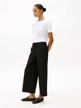 Pantalón negro de corte amplio, tobillero y talle bajo. Confeccionado en tejido antiarrugas de mezcla de viscosa elástica. Presenta cierre de cremallera con enganche oculto, raya marcada en la parte delantera y trasera, y dos bolsillos traseros de ojal.