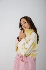 Buzo oversize color crema con estampado de hojas en tonos verde y amarillo, cuello alto con medio cierre metálico y jareta en la cintura para ajustar.
