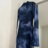 Vestido corto de microtul con estampado abstracto en tonos azules y celestes, cuello alto y mangas largas acampanadas.