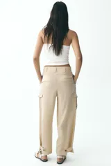 Pantalón color beige de tiro alto con bolsillos delanteros, bolsillos de plastrón con solapa laterales y falsos bolsillos de vivo en la espalda. Bajo acabado con trabilla y botón. Cierre frontal con cremallera y botón.